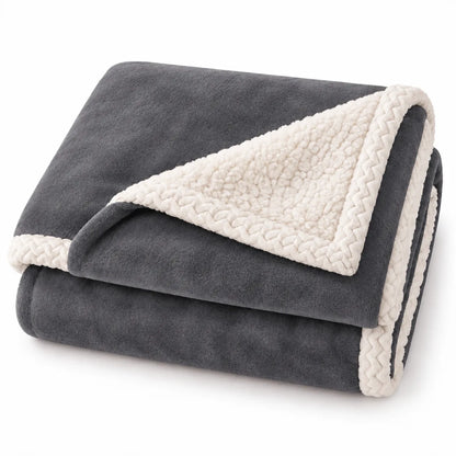 A folded dark gray fleece blanket with a cream sherpa lining and braided trim, shown on a clean white background.