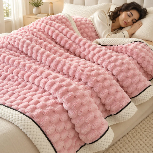 A woman sleeping soundly under a thick, pink, textured bubble blanket with cream-colored borders on a bed in a bright, cozy bedroom.