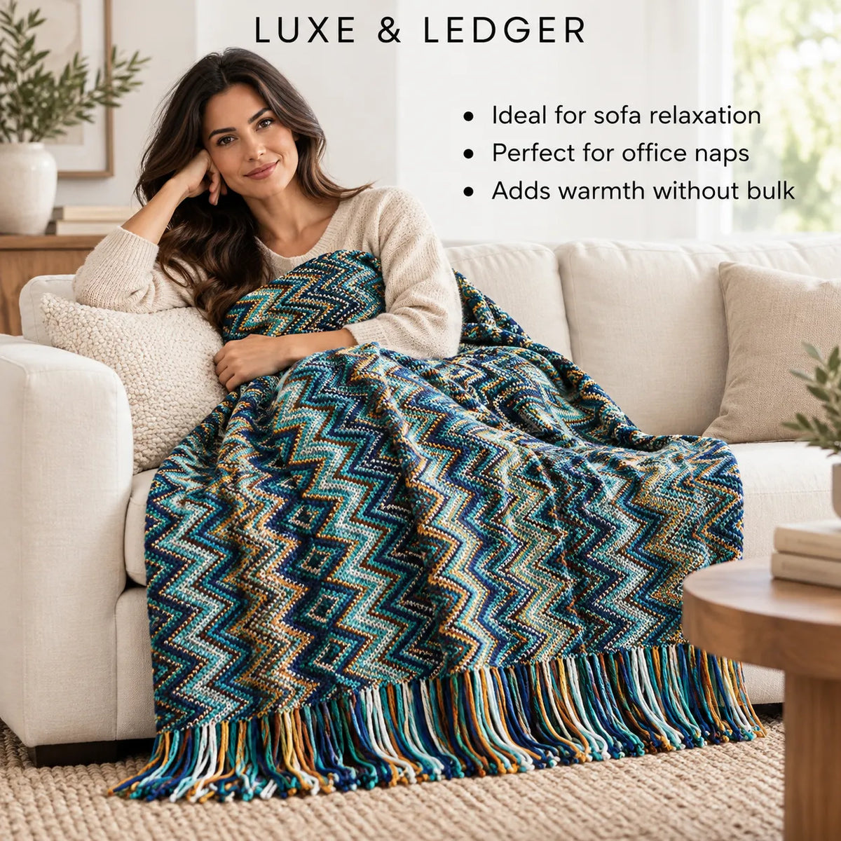 A woman sits on a cream sofa in a bright living room, wrapped in a chunky woven throw blanket with a bold chevron pattern in navy, teal, beige, and orange. Text at the top reads 'LUXE & LEDGER' with bullet points describing the blanket's use cases.
