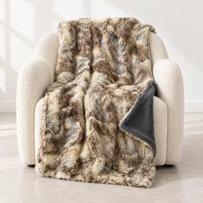 A plush faux-fur throw blanket with a mottled brown, beige, and gray pattern draped over a cream-colored armchair, showing a dark gray sherpa backing.