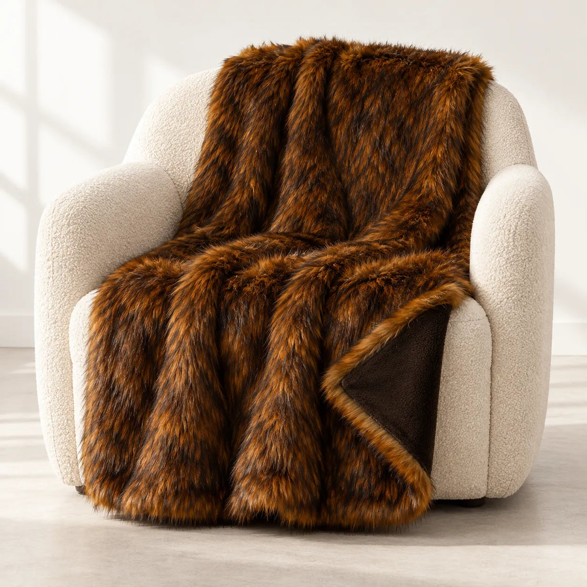 A plush brown faux fur throw blanket with a dark brown reverse side, draped over a cream-colored armchair in a bright, modern room.