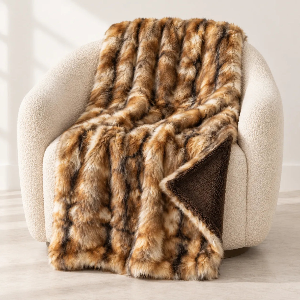 A plush faux fur throw blanket with a brown and tan mottled pattern and a solid dark brown reverse side, draped over a cream-colored armchair in a bright, modern room.