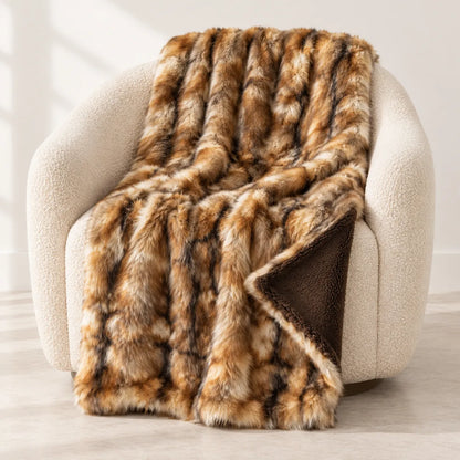 A plush faux fur throw blanket with a brown and tan mottled pattern and a solid dark brown reverse side, draped over a cream-colored armchair in a bright, modern room.