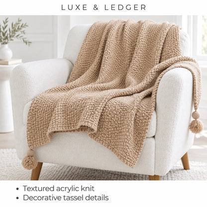 A chunky knit beige throw blanket with tassels draped over a white armchair in a bright, modern room. Text at the top reads 'LUXE & LEDGER', and text at the bottom lists features including 'Textured acrylic knit' and 'Decorative tassel details'.