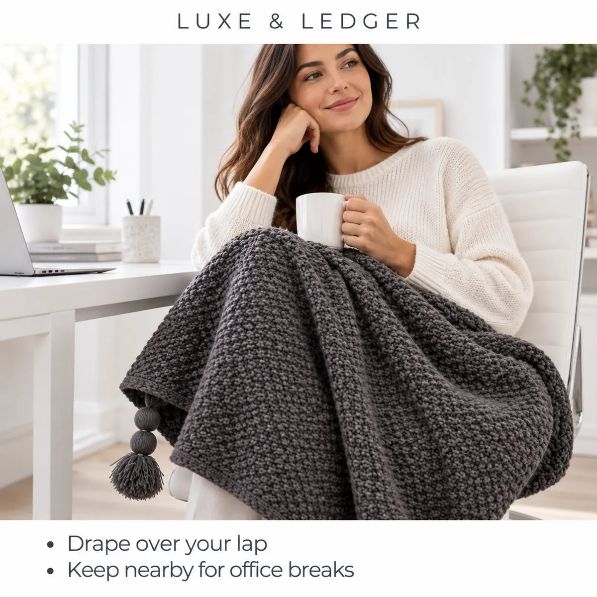A woman in a white knit sweater sits in a bright office chair holding a white mug while draped in a chunky dark gray knit blanket with pom-poms. The image has 'LUXE & LEDGER' branding at the top and marketing text at the bottom.