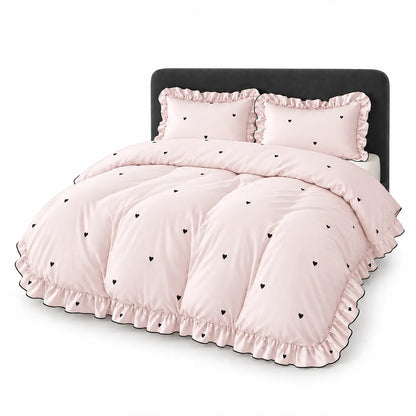 A light pink bedding set with black heart patterns, featuring a comforter and two matching pillow shams with ruffled edges, displayed on a bed with a black headboard against a white background.