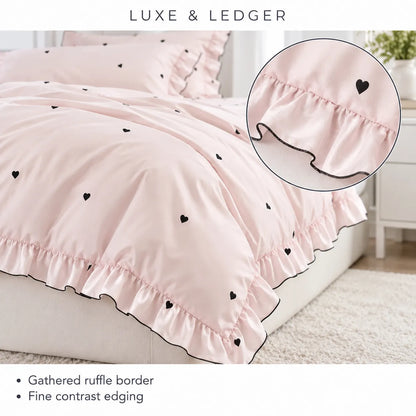 Light pink bedding set with black heart motifs and gathered ruffle borders, shown on a bed with a circular inset highlighting the ruffle detail. Text at top reads 'LUXE & LEDGER' and bullet points at the bottom describe the gathered ruffle border and fine contrast edging.