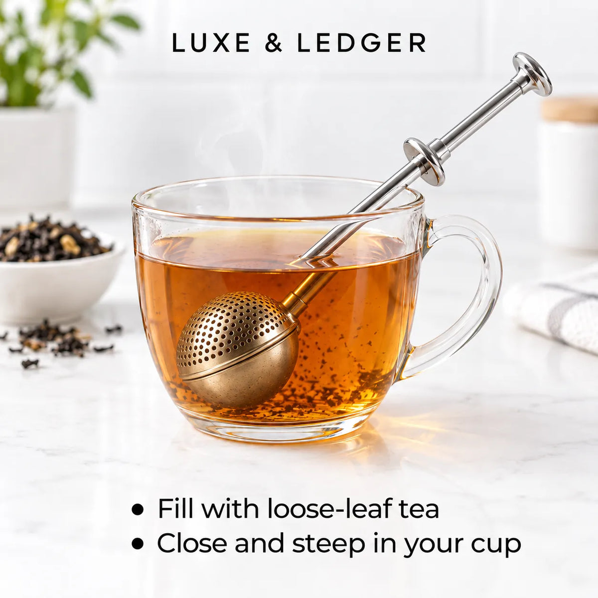 A clear glass teacup filled with amber tea and a metallic ball infuser, with the brand name LUXE & LEDGER at the top and usage text at the bottom on a bright kitchen-like background.