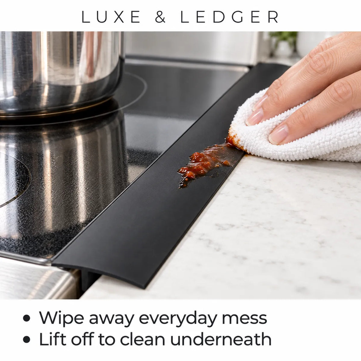 A black silicone kitchen counter drip tray shown in a real kitchen setting, with a hand wiping a stained area with a white towel. The text at the top reads 'LUXE & LEDGER' and the text at the bottom says 'Wipe away everyday mess' and 'Lift off to clean underneath'.
