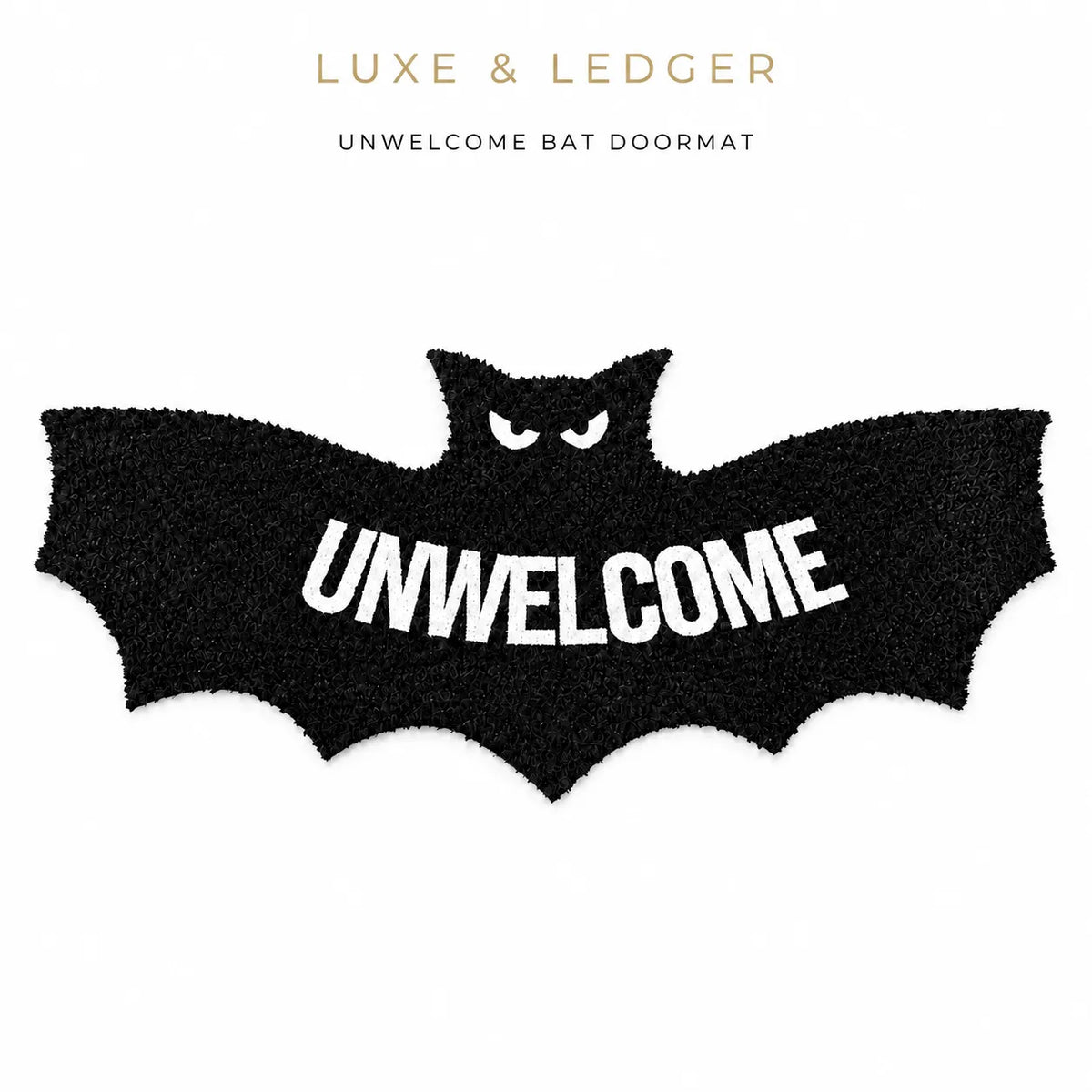 A black bat-shaped doormat with white fuzzy eyes and the word 'UNWELCOME' in large white letters across the center, shown on a white background with 'LUXE & LEDGER' and 'UNWELCOME BAT DOORMAT' text above.