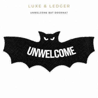 A black bat-shaped doormat with white fuzzy eyes and the word 'UNWELCOME' in large white letters across the center, shown on a white background with 'LUXE & LEDGER' and 'UNWELCOME BAT DOORMAT' text above.