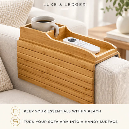 A bamboo sofa arm tray organizer with a cup holder and remote slot, shown resting on a light beige couch. The top of the tray holds a white mug and a white remote control.