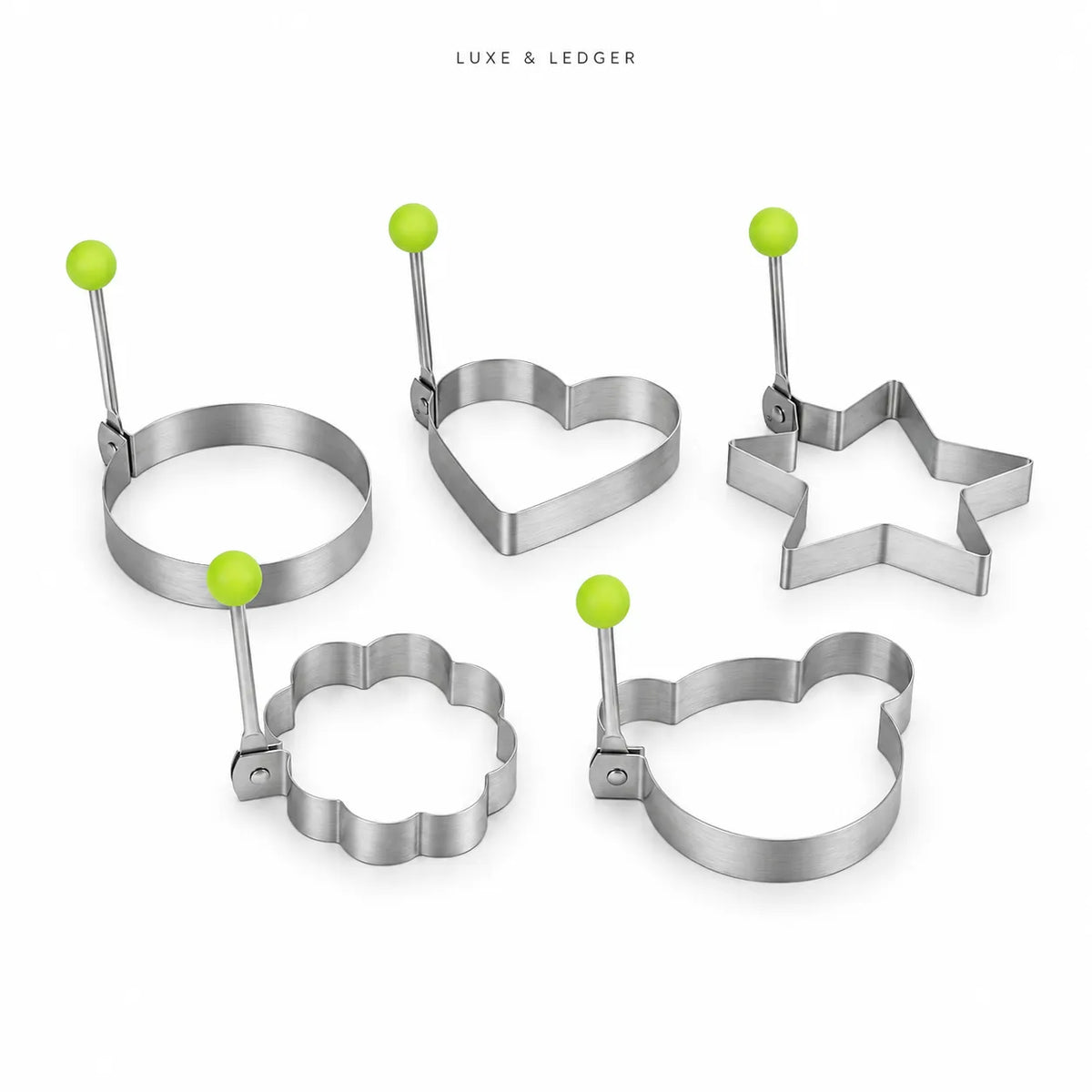 Five metal cookie cutters in ring, heart, star, flower, and bear shapes, each with a bright green spherical handle, arranged on a white background. The brand name 'LUXE & LEDGER' is printed at the top center.