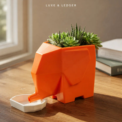 An orange geometric elephant-shaped planter with a white dish in front, holding small green succulents, set on a wooden table in a softly lit indoor setting. The text 'LUXE & LEDGER' appears at the top.