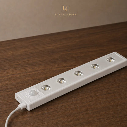 A white 5-light under-cabinet LED strip light with a built-in motion sensor, shown plugged into a wooden surface with a neutral background. The brand name 'LUXE & LEDGER' is visible at the top.