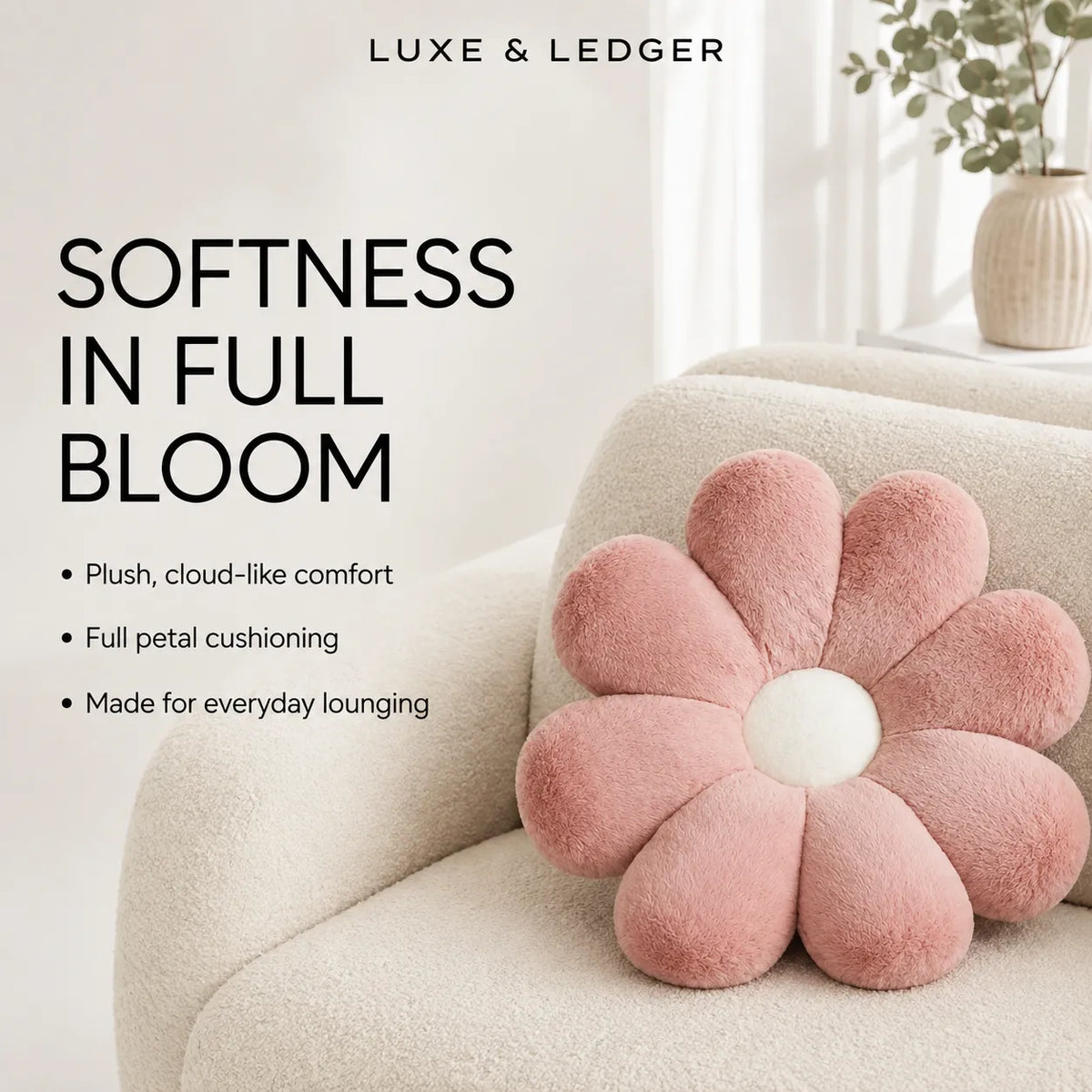 A pink flower-shaped throw pillow with a white center resting on a cream bouclé armchair in a bright, modern room. Text on the left reads 'LUXE & LEDGER' and 'SOFTNESS IN FULL BLOOM' with bullet points describing the plush cushion.