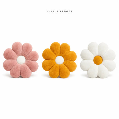 Three plush flower-shaped cushions in pink, mustard yellow, and white are arranged on a clean white background, with the brand name 'LUXE & LEDGER' printed above.
