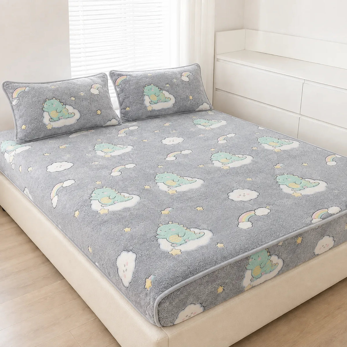 A gray plush bed sheet set with matching pillowcases, featuring a cute cartoon cloud and dinosaur pattern, styled on a bed in a bright, modern bedroom.