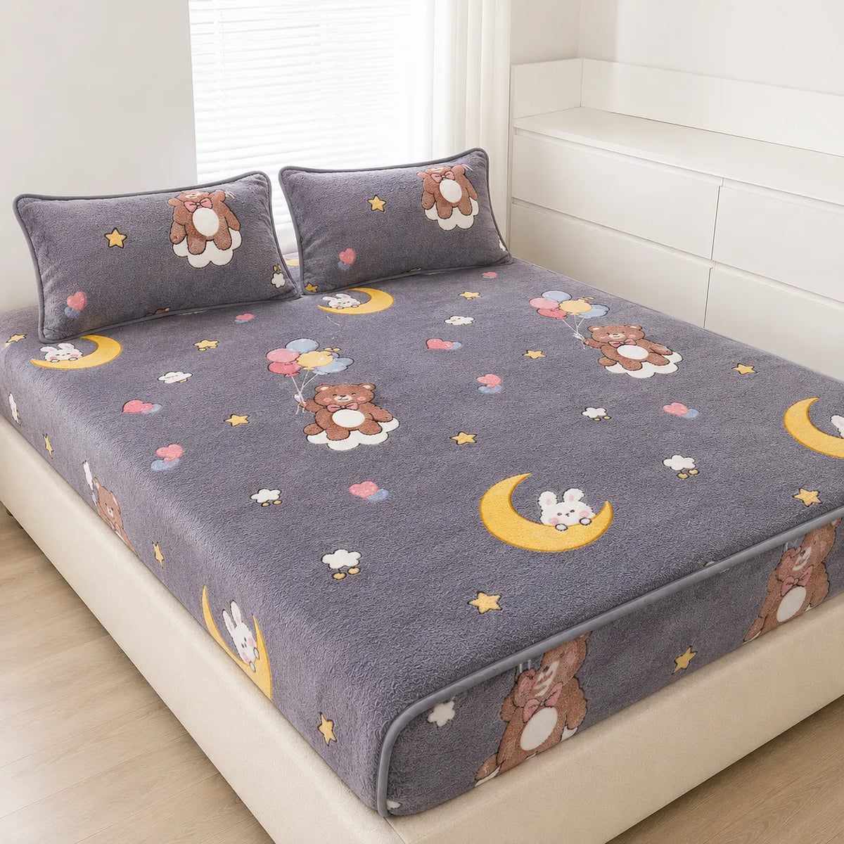 A gray plush bed sheet set with matching pillowcases, featuring a cute cartoon pattern of bears, rabbits, moons, stars, and balloons, shown on a bed in a bright bedroom.