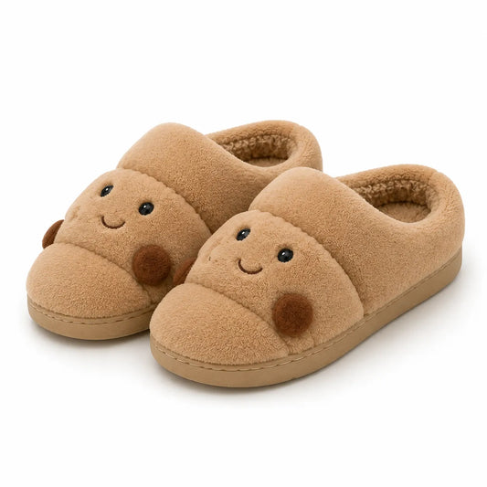 A pair of plush tan slipper shoes with a cute cartoon face on the toe, featuring embroidered eyes and a stitched smile, set against a plain white background.