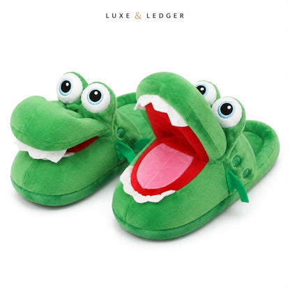 A pair of green plush crocodile slippers with large cartoon eyes and open mouths showing white teeth, red interiors, and pink tongues. The brand name 'LUXE & LEDGER' is printed at the top center on a white background.