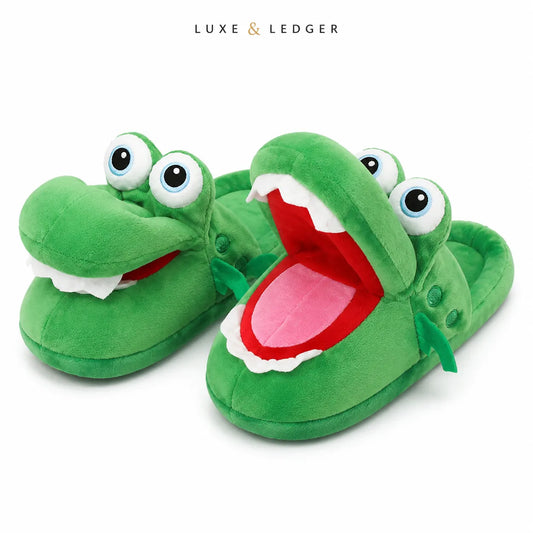 A pair of green plush crocodile slippers with large cartoon eyes and open mouths showing white teeth, red interiors, and pink tongues. The brand name 'LUXE & LEDGER' is printed at the top center on a white background.