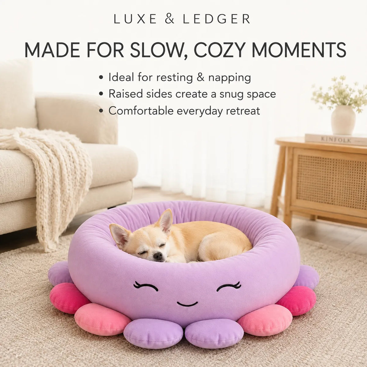 A small tan dog rests inside a round lavender pet bed with pink and purple octopus-like legs and a smiling face. The scene is set in a softly lit living room with a sofa, blanket, side table, and text at the top reading 'LUXE & LEDGER MADE FOR SLOW, COZY MOMENTS'.