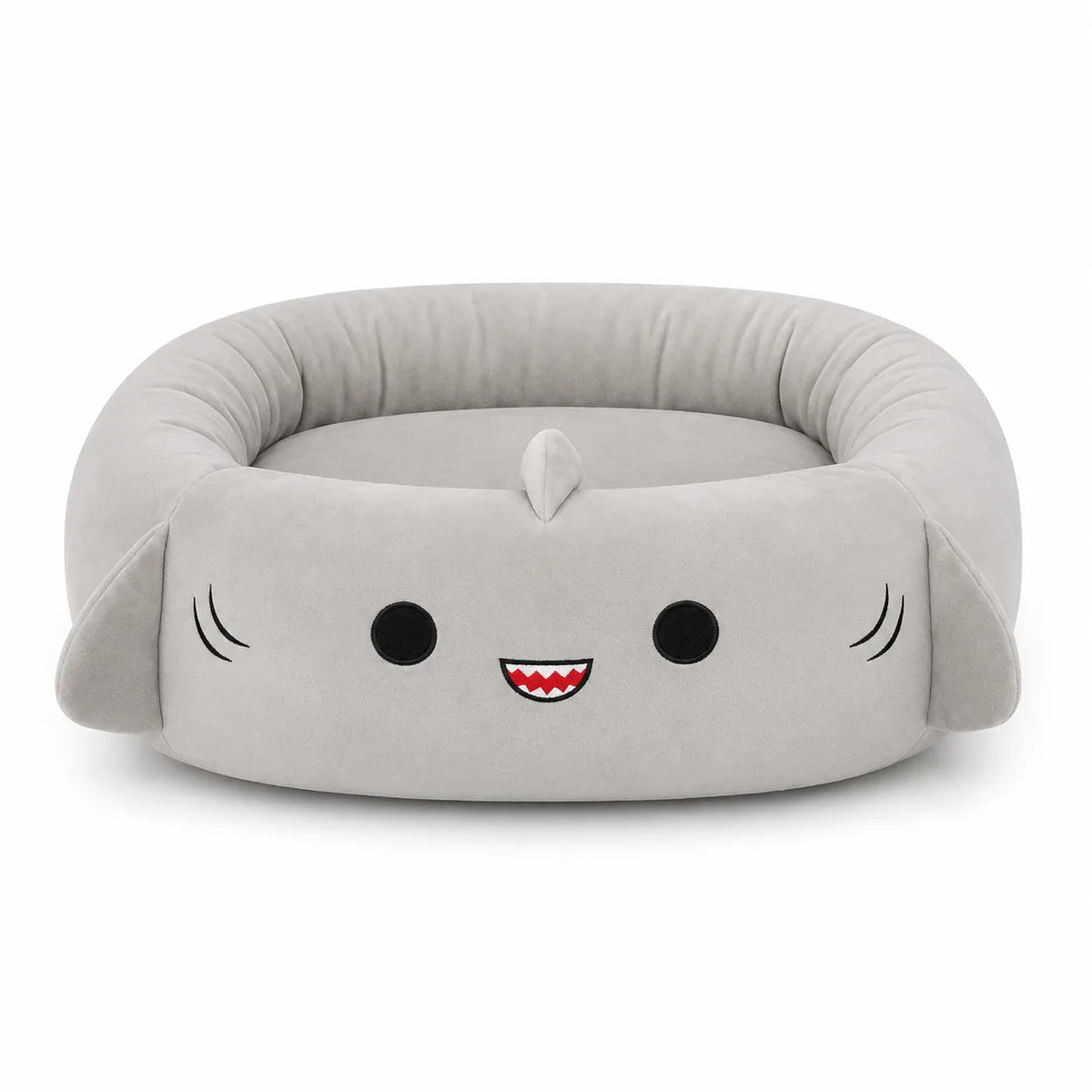 A plush shark-shaped pet bed in light gray fabric, featuring embroidered black eyes, a red and white smiling mouth, and small black whisker details on a clean white background.