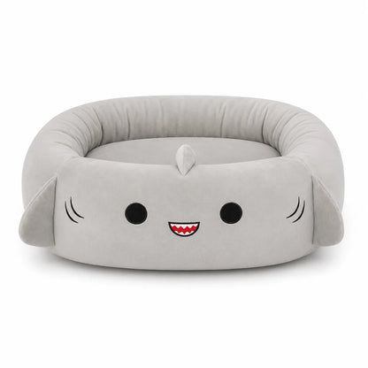 A plush shark-shaped pet bed in light gray fabric, featuring embroidered black eyes, a red and white smiling mouth, and small black whisker details on a clean white background.