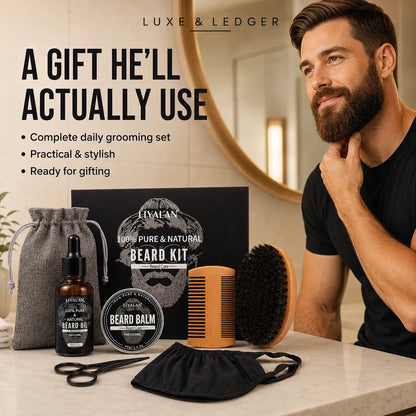 A man with a full beard sits beside a grooming gift set on a bathroom counter. The set includes a beard oil bottle, beard balm tin, comb, brush, face mask, scissors, and a drawstring pouch, with a branded box behind them.