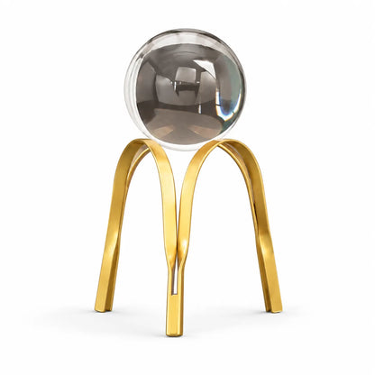 A modern decorative sculpture featuring a polished metallic gold double-arch stand supporting a large, reflective silver glass sphere, set against a seamless white background.