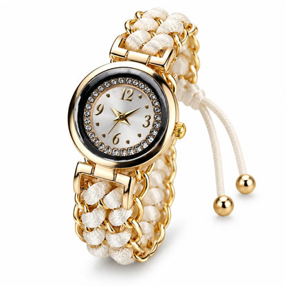 A women's gold-tone watch with a round crystal-studded bezel, white dial with gold numerals, and a braided white cord bracelet with gold links and adjustable cord ends.
