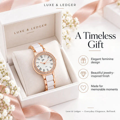 Luxe & Ledger women's watch displayed in an open white presentation box with blush pink ribbon and floral accents. The watch has a white strap, a white dial with black Roman numerals, and a rose gold case accented with clear crystals.
