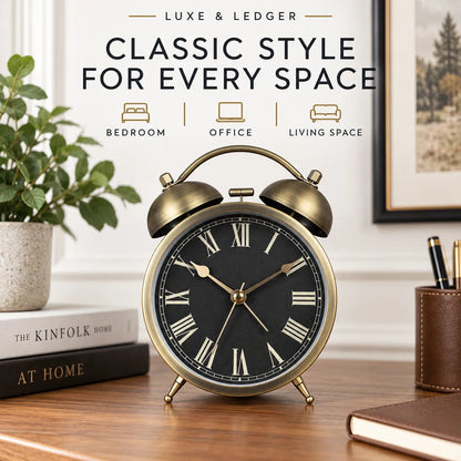 A classic-style twin-bell alarm clock with a brass-gold metal body and a black face with Roman numerals, displayed on a wooden desk in a styled home office setting. The background features a white wall with decorative text reading 'LUXE & LEDGER CLASSIC STYLE FOR EVERY SPACE' and icons for bedroom, office, and living space.