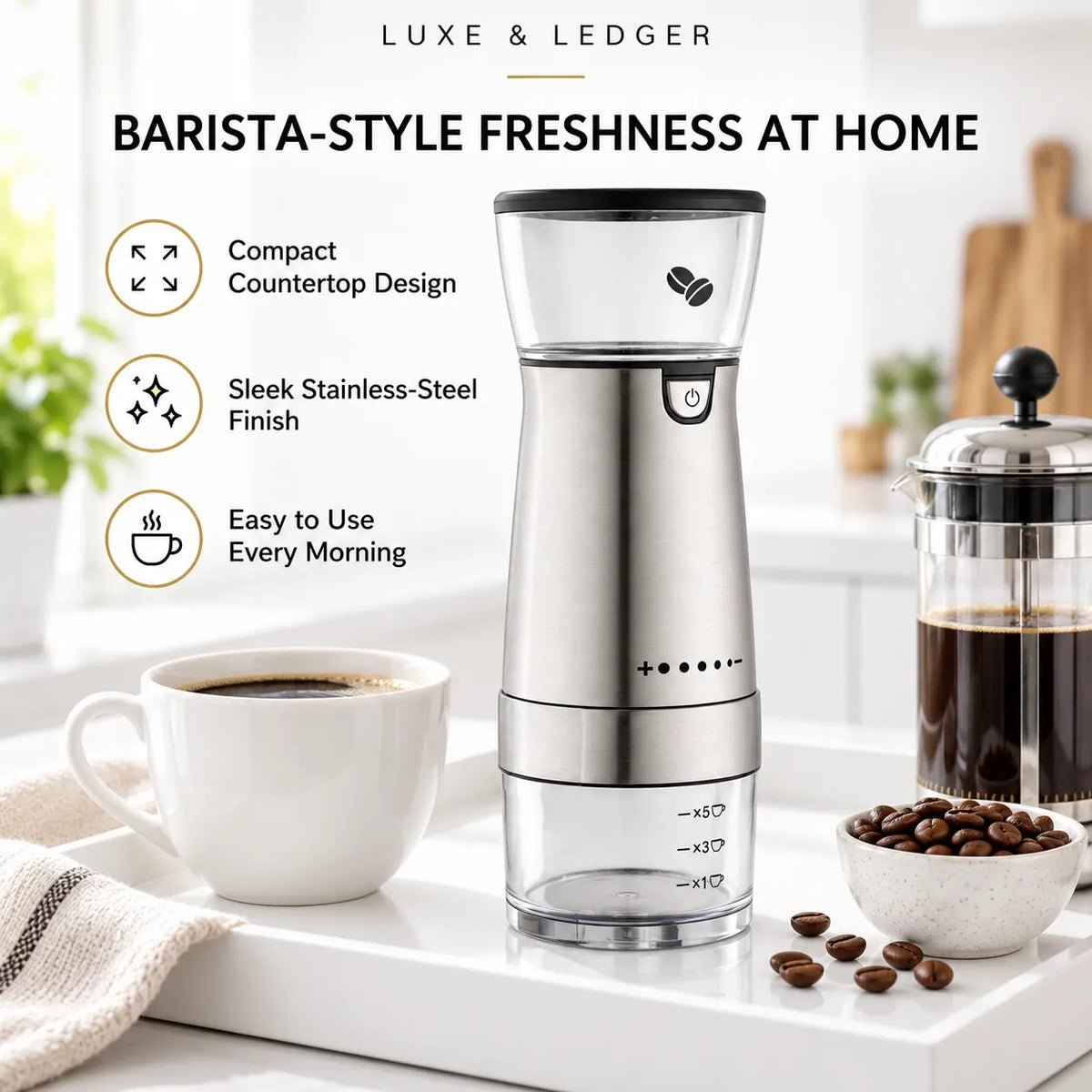 A Luxe & Ledger barista-style handheld coffee grinder stands on a white countertop beside a cup of coffee, a bowl of coffee beans, and a French press. The product is shown in a bright kitchen setting with marketing text highlighting compact countertop design, stainless-steel finish, and ease of use.