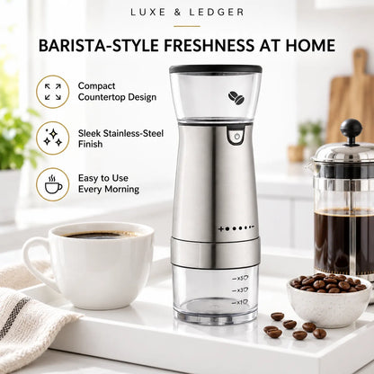 A Luxe & Ledger barista-style handheld coffee grinder stands on a white countertop beside a cup of coffee, a bowl of coffee beans, and a French press. The product is shown in a bright kitchen setting with marketing text highlighting compact countertop design, stainless-steel finish, and ease of use.