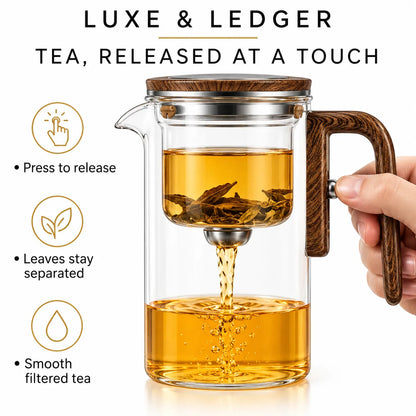 A clear glass teapot with a dark wood handle and lid, shown with a metal infuser filter and amber tea inside. A hand holds the handle on the right.