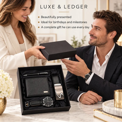 A man and woman seated at a table present a luxury gift set. The open black box contains a black leather wallet, a silver-tone belt with a black strap, a black watch with a silver bezel, and a black pen.