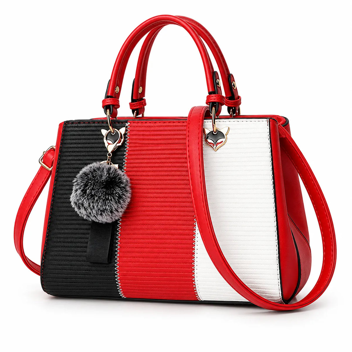 A structured handbag with a color-blocked design in black, red, and white, featuring dual top handles, a shoulder strap, a gray faux-fur pom-pom charm, and heart-shaped metal hardware.
