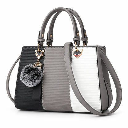 A structured handbag with a three-tone color-blocked design in black, gray, and white textured panels, featuring gray leather handles, a shoulder strap, a gray faux-fur pom-pom charm, and a small fox-head metal logo.