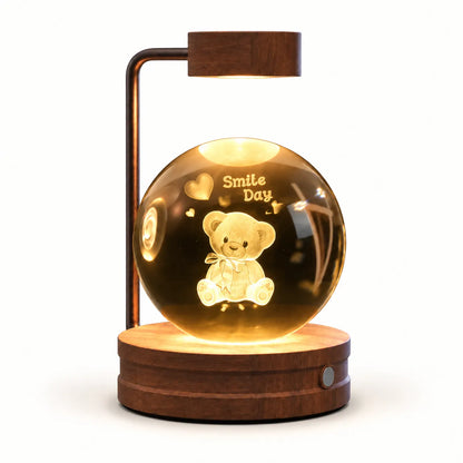 A wooden table lamp with a glowing clear glass globe containing a teddy bear and the words 'Smile Day,' mounted on a round wooden base with a curved wooden arm and rectangular lamp head.