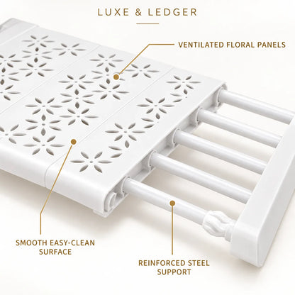 White plastic shower caddy with labeled callouts reading 'LUXE & LEDGER', 'VENTILATED FLORAL PANELS', 'SMOOTH EASY-CLEAN SURFACE', and 'REINFORCED STEEL SUPPORT' on a light beige background.