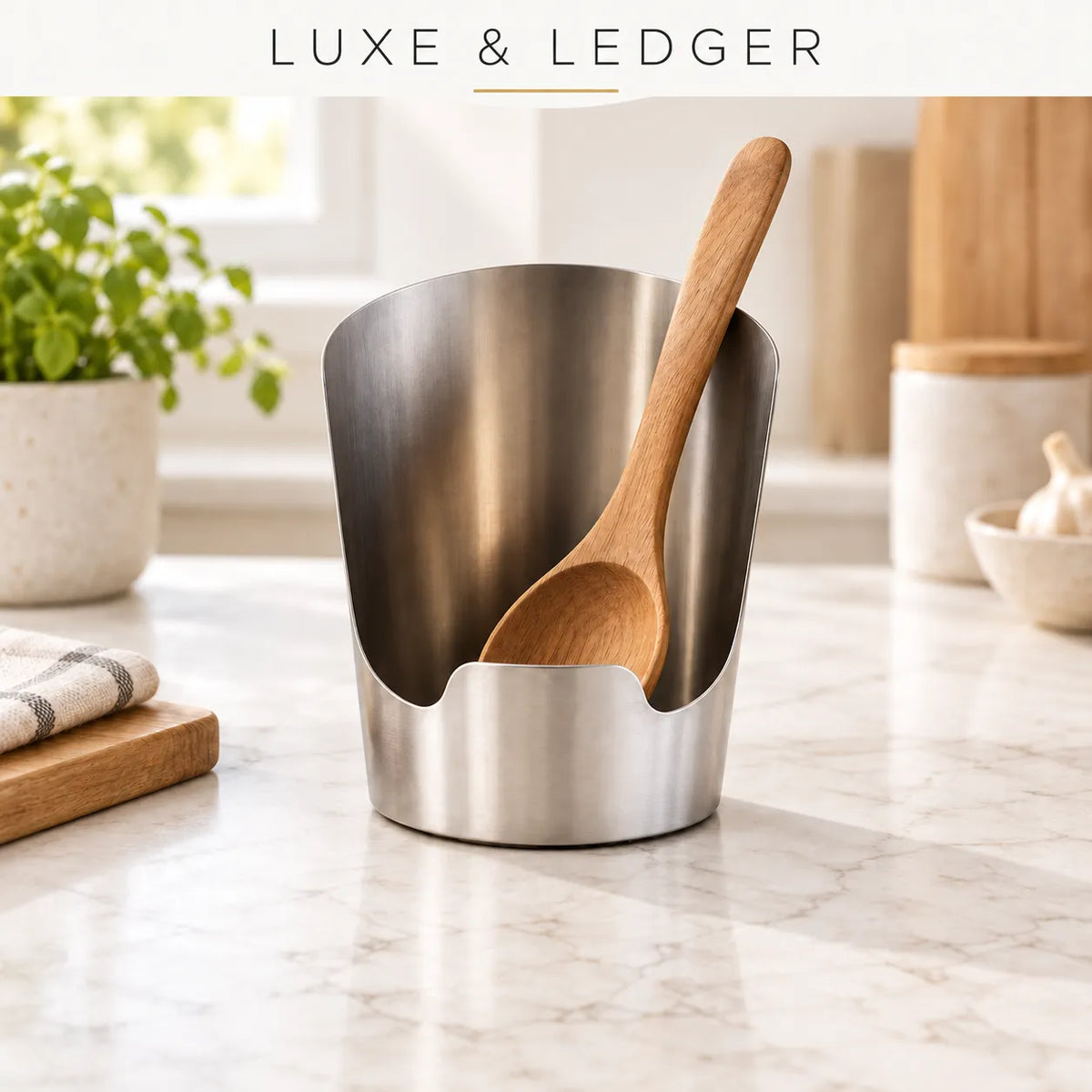 A stainless steel kitchen utensil holder with a wooden spoon inside, set on a light marble countertop in a bright kitchen. The text 'LUXE & LEDGER' appears at the top.