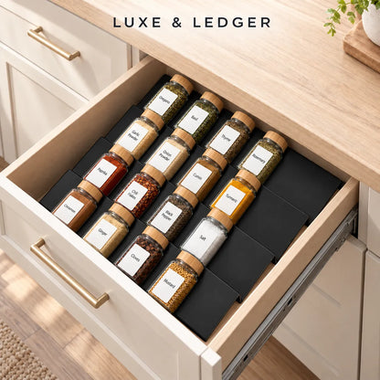 An open kitchen drawer organizer holding multiple labeled spice jars arranged in a black tray, set inside a light wood and cream cabinet. The text 'LUXE & LEDGER' appears at the top.