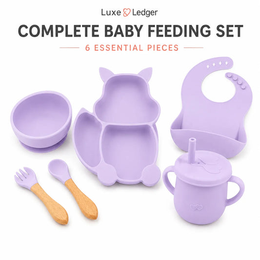Luxe Ledger baby feeding set in lavender purple, including a silicone bowl, divided plate, bib, sippy cup, fork, and spoon, with wooden-handled utensils on a white background.