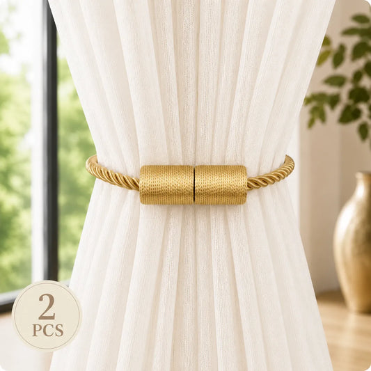 A pair of gold curtain tiebacks with twisted rope sides and a textured cylindrical center, shown tied around a white curtain in a bright room. A circular '2 PCS' badge is in the lower-left corner.