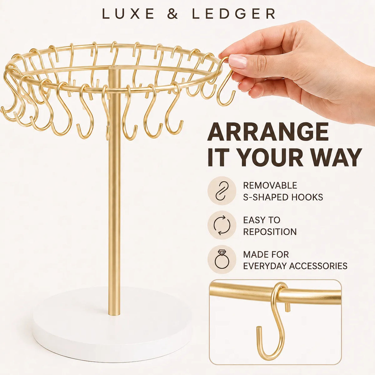 Gold jewelry stand with a white circular base and multiple S-shaped hooks, shown with a hand adjusting a hook. Text reads 'LUXE & LEDGER' and 'ARRANGE IT YOUR WAY' with feature icons.