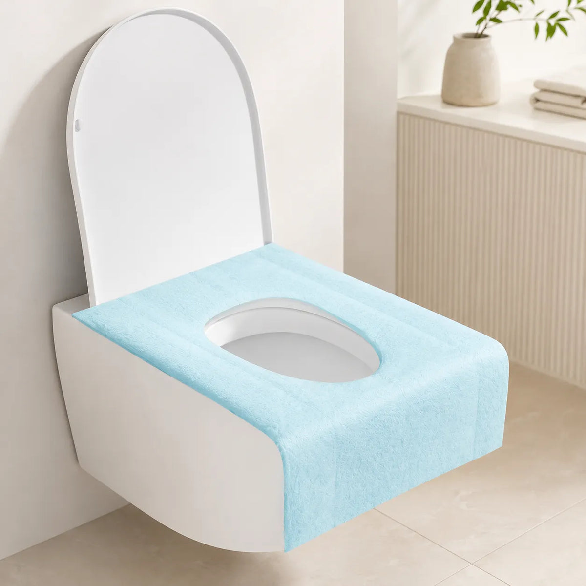 A light blue toilet training pad or potty cover with an oval cutout, shown fitted on a white wall-mounted toilet in a clean, modern bathroom setting.