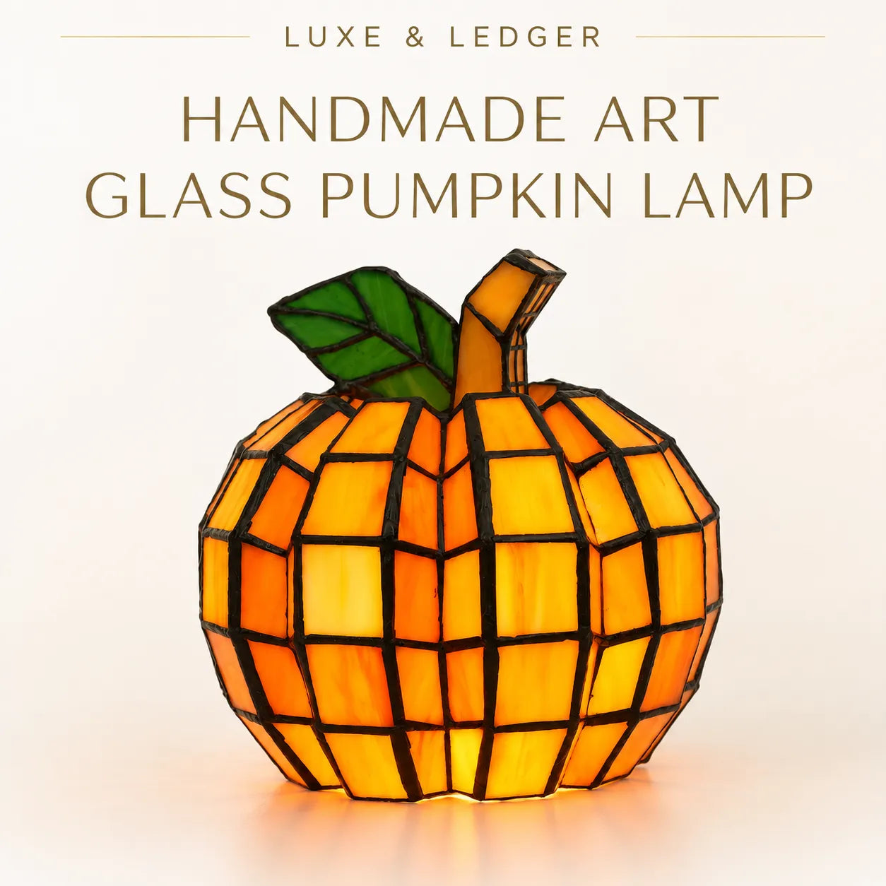 A handmade geometric glass pumpkin lamp with orange and yellow stained-glass panels, a green leaf, and a brown stem, shown against a light beige background with the text 'LUXE & LEDGER HANDMADE ART GLASS PUMPKIN LAMP' at the top.