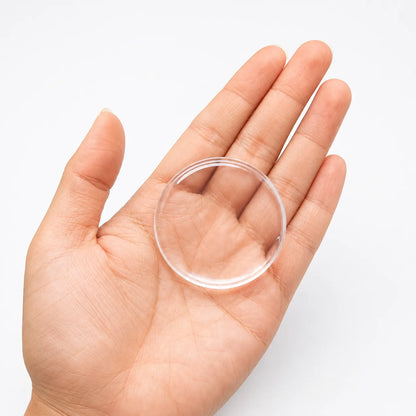 A clear, round plastic or acrylic disc held in the palm of a hand against a plain white background.